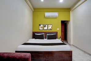 Een hotelkamer met een bed, nachtkastje, airconditioning en een deur.