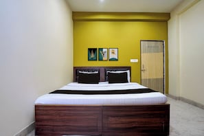 Een enkel bed met een donker hoofdbord en witte beddengoed in een kamer met gele muren.