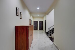 A hallway with a wooden reception desk, two framed pictures on the wall, and a staircase with a metal railing. - Super Hotel O Samne Ghat (Varanasi)