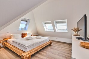 A bedroom with a sloped ceiling, a wooden bed frame, a white mattress, and two windows. - Holiday apartment with 3 bedrooms (Hörnum)