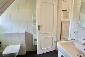 Un baño con inodoro, una puerta blanca, un lavamanos blanco y un perchero para toallas.