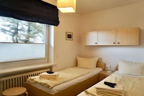Una habitación con dos camas, una ventana con persianas, un radiador, una mesita y un armario.