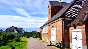 Ein Backsteinhaus mit Kruzifix auf dem Dach, einem gepflasterten Weg und einer Bank.