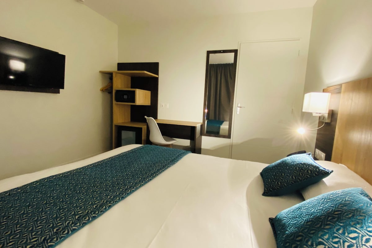 A hotel room with a bed, a desk, a chair, and a wardrobe.
