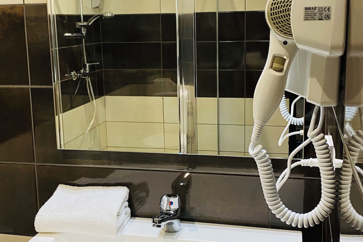 A bathroom with a shower, a sink, and a hairdryer.