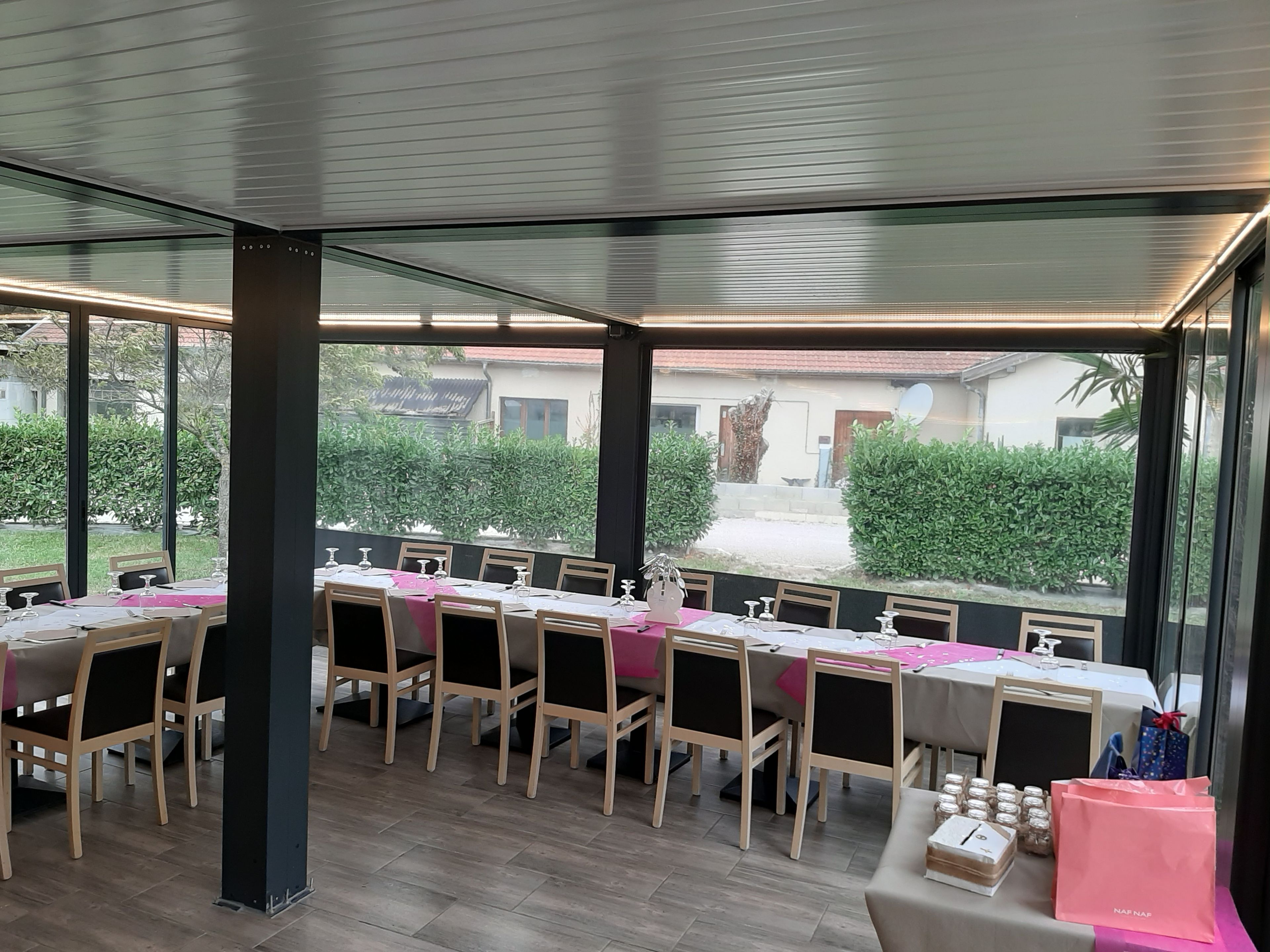 Ein Restaurant mit einem langen Esstisch, großen Fenstern und Blick ins Freie.