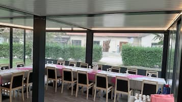 Ein Restaurant mit einem langen Esstisch, großen Fenstern und Blick ins Freie.