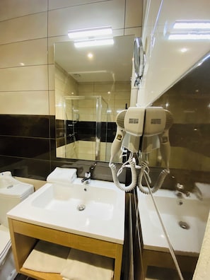 A bathroom with a white sink, a mirror, and a hairdryer mounted on the wall. - Appart'hôtel Martinez (Grenay)