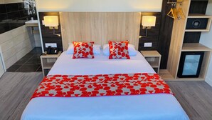 A hotel room with a large bed, two bedside tables, a nightstand, a built-in mini-fridge, and a wall-mounted lamp. - Appart'hôtel Martinez (Grenay)