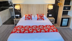 A hotel room with a large bed, two bedside tables, a nightstand, a built-in mini-fridge, and a wall-mounted lamp. - Appart'hôtel Martinez (Grenay)