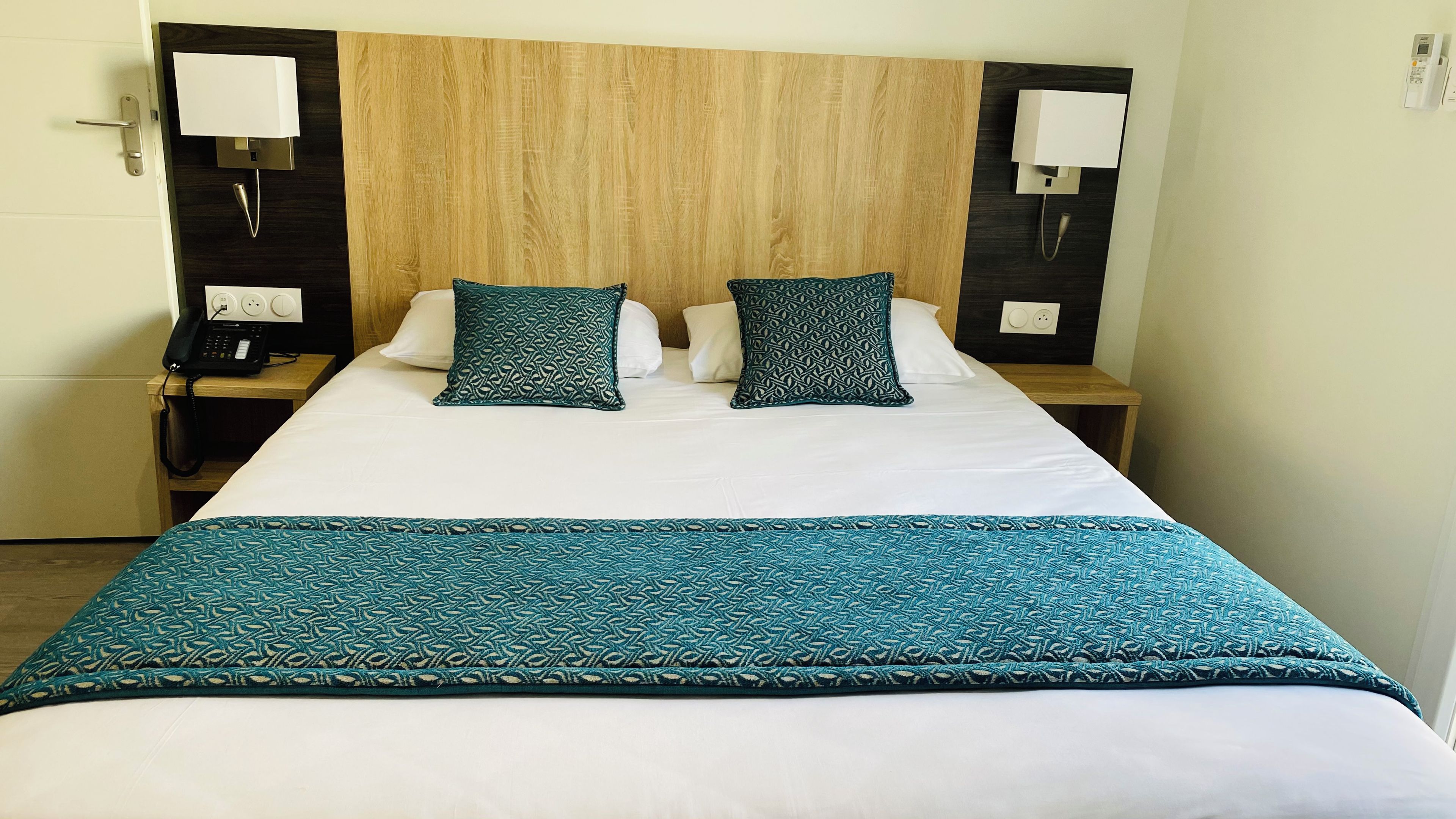 Habitación de hotel con cama, dos mesitas de noche, teléfono y lámpara de pared.