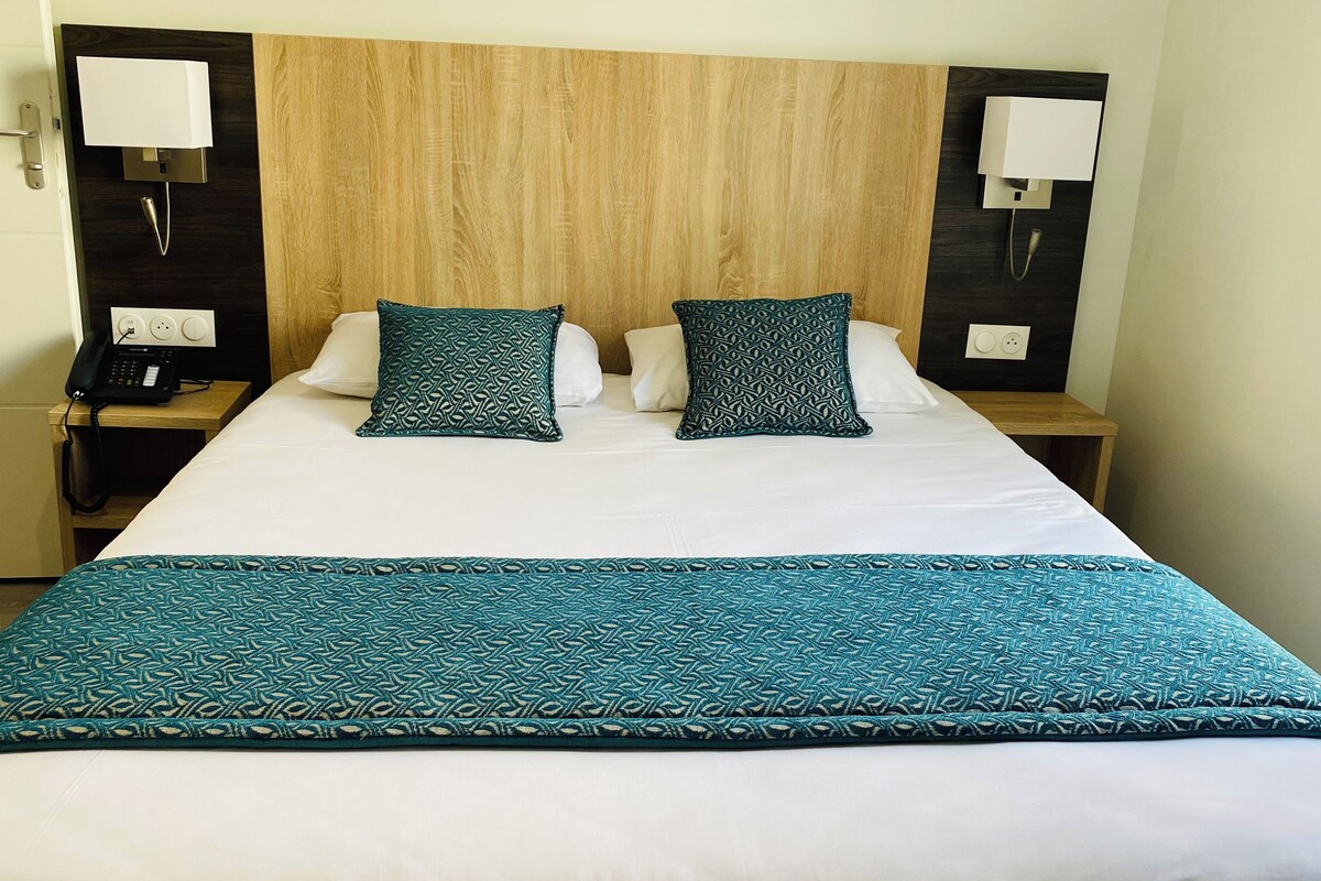 A hotel room with a bed, two bedside tables, a telephone, and a wall-mounted light fixture.