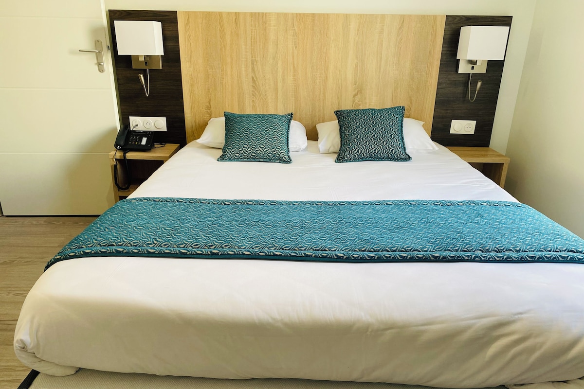 A hotel room with a bed, two bedside tables, a telephone, and a wall-mounted lamp.