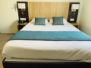 A hotel room with a bed, two bedside tables, a telephone, and a wall-mounted lamp. - Appart'hôtel Martinez (Grenay)