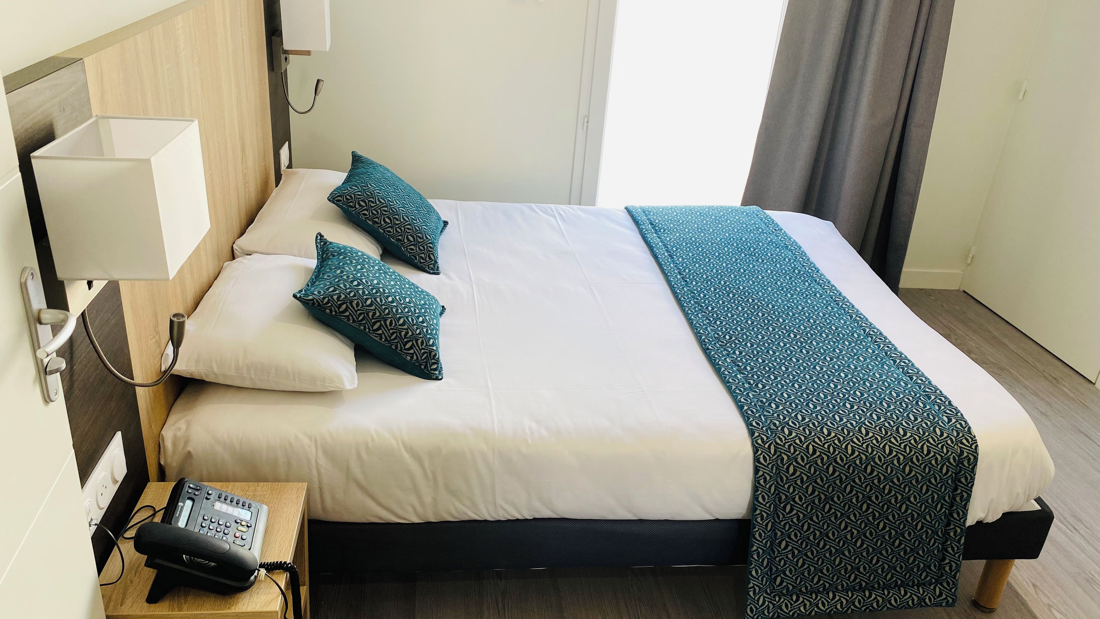 Ein Hotelzimmer mit einem Bett, Kissen, einem Nachttisch mit Telefon und einer Lampe.
