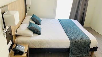 Ein Hotelzimmer mit einem Bett, Kissen, einem Nachttisch mit Telefon und einer Lampe.