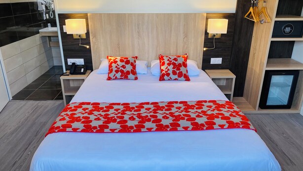 A hotel room with a large bed, two bedside lamps, a minibar, and a small refrigerator. - Appart'hôtel Martinez (Grenay)
