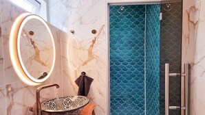 Casa de banho com toucador em mármore, lavatório decorativo em forma de taça e chuveiro com padrão de azulejos em forma de escama de peixe azul.