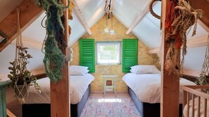 Quarto de sótão acolhedor com duas camas, uma mesinha e uma janela com venezianas verdes.
