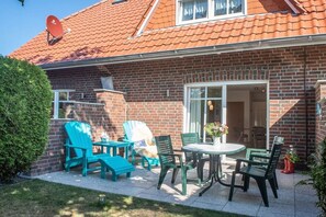 Ein Ziegelhaus mit einem Ziegeldach, einer Satellitenschüssel und einer Terrasse mit Gartenmöbeln.