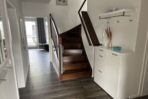 Eine Treppe führt zu einer Zwischenebene mit einem weißen Schrank und einem kleinen Tisch mit einer Vase.
