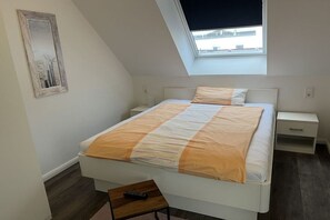 A bedroom with a bed, bedside tables, a nightstand, a window, and a skylight. - Holiday apartment with 1 bedroom (Norderney)