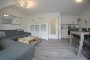 A modern living room with a grey sofa, a wooden coffee table, and a dining area with a table and chairs. - Holiday apartment with 1 bedroom (Norderney)