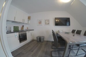 A modern kitchen with white cabinets, a built-in oven, and a dining area with a table and chairs. - Holiday apartment with 1 bedroom (Norderney)