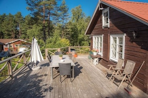 A wooden deck with a table and chairs, surrounded by a railing, overlooking a forested area. - Holiday home with 3 bedrooms (Loftahammar)