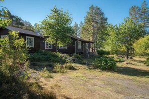 A rustic cabin with a porch, surrounded by dense greenery and trees.