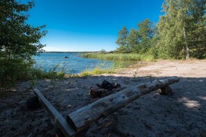 A sandy beach with a wooden log and rocks, surrounded by trees and a calm body of water.