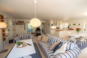 A modern living room with a sofa set, a dining table, and a kitchen area with cabinets and a stove. - Holiday home with 3 bedrooms (Loftahammar)