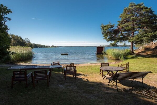 A lakeside outdoor seating area with tables and chairs, a dock, and a tree.