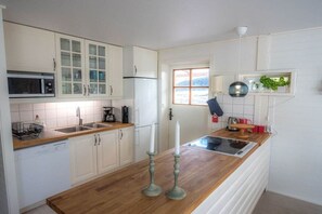 A kitchen with white cabinets, a microwave, a refrigerator, a sink, and a window. - Holiday home with 3 bedrooms (Loftahammar)