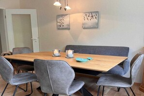 A dining area with a wooden table, grey upholstered chairs, and two wall-mounted light fixtures. - Holiday apartment on Damenpfad (Wangerooge)