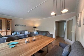 A modern living room with a wooden dining table, grey sofas, and a cabinet. - Holiday apartment on Damenpfad (Wangerooge)