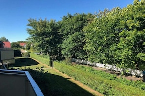 A residential area with a well-maintained lawn, a white fence, and a variety of trees. - Holiday apartment on Damenpfad (Wangerooge)