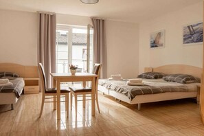 A bedroom with a bed, a sofa, a dining table with chairs, and a window with curtains. - One-bedroom guesthouse in Poland (Grzybowo \/ Kolberg)
