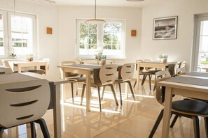 A bright dining area with multiple tables and chairs, large windows with natural light, and a view of greenery outside. - One-bedroom guesthouse in Poland (Grzybowo \/ Kolberg)