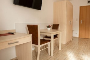 A room with a wooden desk, two chairs, a television mounted on the wall, and a wardrobe. - One-bedroom guesthouse in Poland (Grzybowo \/ Kolberg)