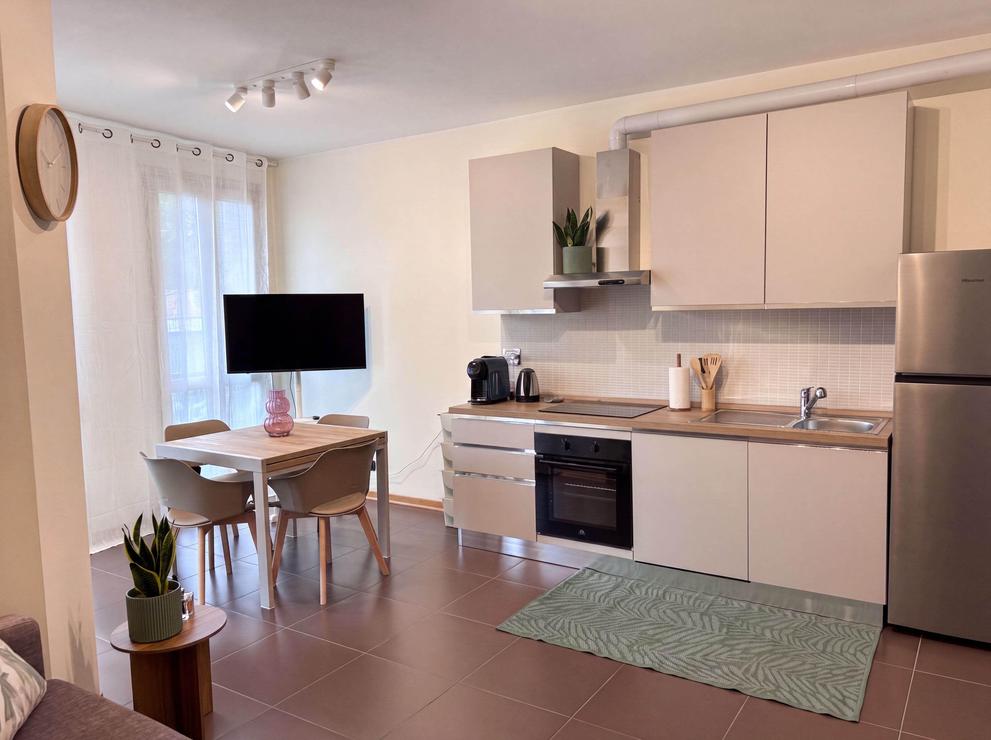 A modern kitchen with a dining area, a flat-screen TV, and a stainless steel refrigerator.