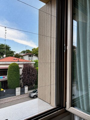 A window with a view of a residential street, a neatly trimmed hedge, and a parked car. - Bright & comfortable apartment in Carpi—your perfect base for exploring Italy (Carpi)