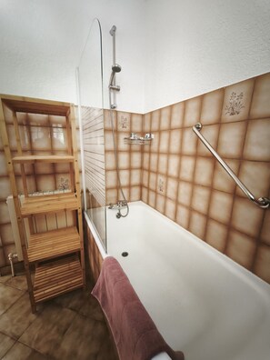Ein Badezimmer mit einer Badewanne, einem Holzregal und einer Duschkabine aus Glas.