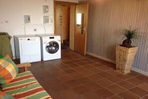 Une buanderie équipée de deux machines à laver, avec une porte en bois, une plante en pot et un canapé à rayures.