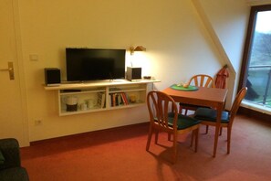 A dining area with a table, chairs, a television on a shelf, and a window. - Holiday apartment with 2 bedrooms (Borkum)