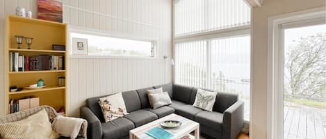 A cozy living room with a grey sofa, a wicker chair, a white coffee table, and a bookshelf.