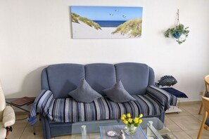 Uma sala de estar com sofá, mesa de centro com flores, quadro na parede e planta pendente.