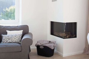 Une pièce d’angle avec un canapé, une petite poubelle noire et une cheminée.