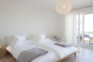 Ein Schlafzimmer mit einem Doppelbett, einem Nachttisch, einem Sessel und einem großen Fenster.