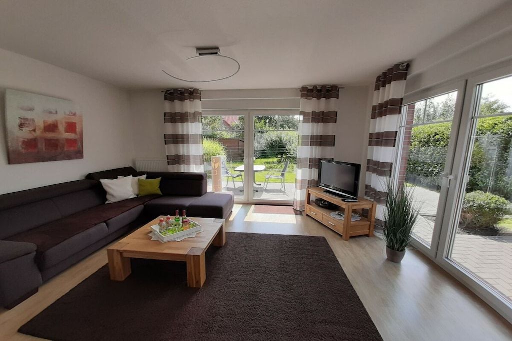 Un salon moderne comprenant un canapé, une table basse, un meuble pour la télévision et offrant une vue sur l’extérieur grâce à de grandes fenêtres.